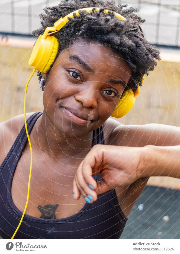 Zufriedene afroamerikanische Frau, die auf der Straße Musik hört meloman Kopfhörer zuhören benutzend Melodie Audio verträumt genießen sportlich Stil Porträt
