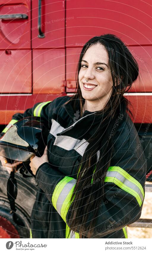 Glückliche Feuerwehrfrau in der Nähe des Feuerwehrautos stehend Frau Feuerwehrmann Lastwagen Uniform Schutzhelm Beruf behüten Job Lächeln positiv jung