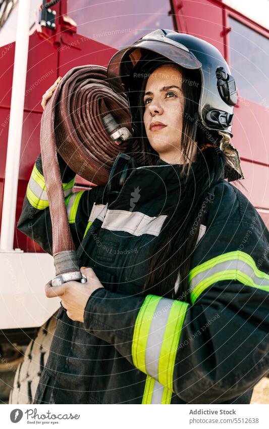 Junge Feuerwehrfrau trägt Feuerwehrschlauch Frau Feuerwehrmann führen Schlauch Feuerwehrauto Beruf behüten Held Mut Notfall jung Schwarzes Haar Sicherheit