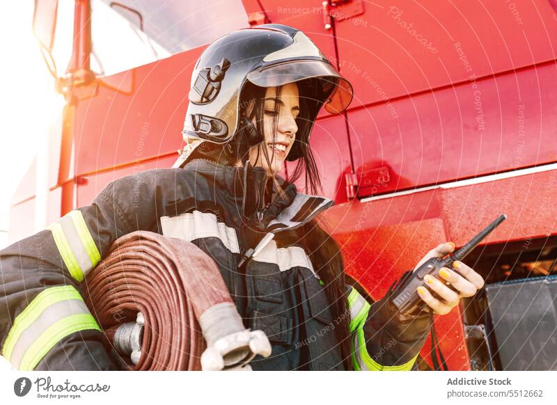 Feuerwehrfrau mit Funkgerät in der Nähe des Feuerwehrautos Frau Feuerwehrmann Walkie-Talkie Radio Kommunizieren Schlauch Lastwagen Notdienst Job jung