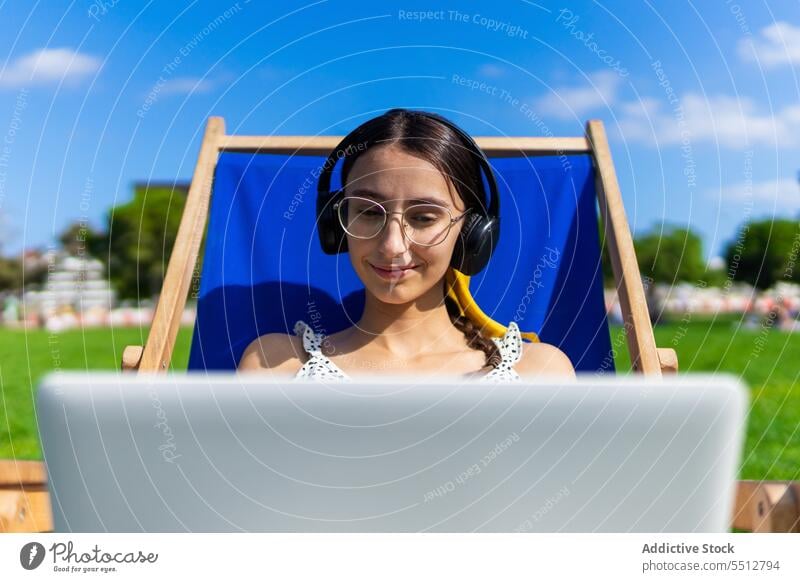 Lächelnde Frau mit Laptop im Kopfhörer Musik zuhören sich[Akk] entspannen Sommer benutzend Glück genießen Gerät Apparatur Stuhl jung Klang Audio Kälte Computer