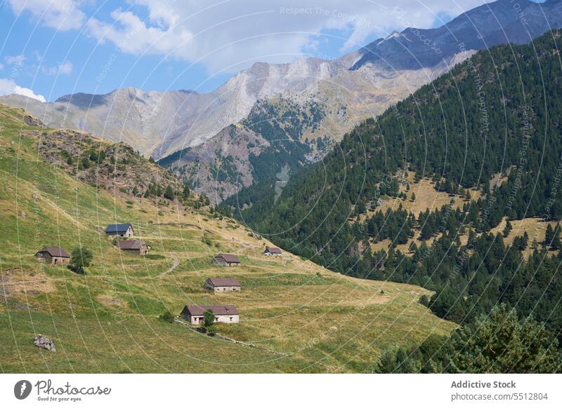 Siedlung auf einem grasbewachsenen grünen Hügel vor einer Bergkulisse unter blauem Himmel malerisch Berge u. Gebirge Pyrenäen Ambitus Landschaft Natur Hochland