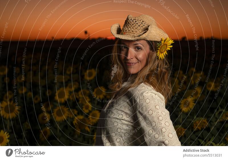 Lächelnde Frau mit Strohhut in einem Sonnenblumenfeld stehend Feld positiv Landschaft Sonnenuntergang Sommer genießen ländlich Natur Blume Glück Umwelt Inhalt