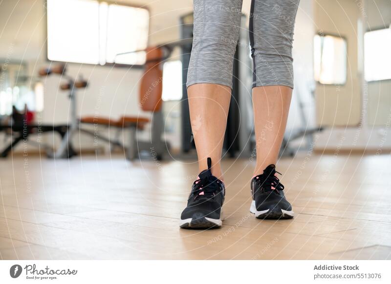 Unerkennbare junge Frau steht mit Schuhen auf dem Boden einer Turnhalle bei Tageslicht Athlet Übung Fitnessstudio Training Gerät Maschine Leggings stehen