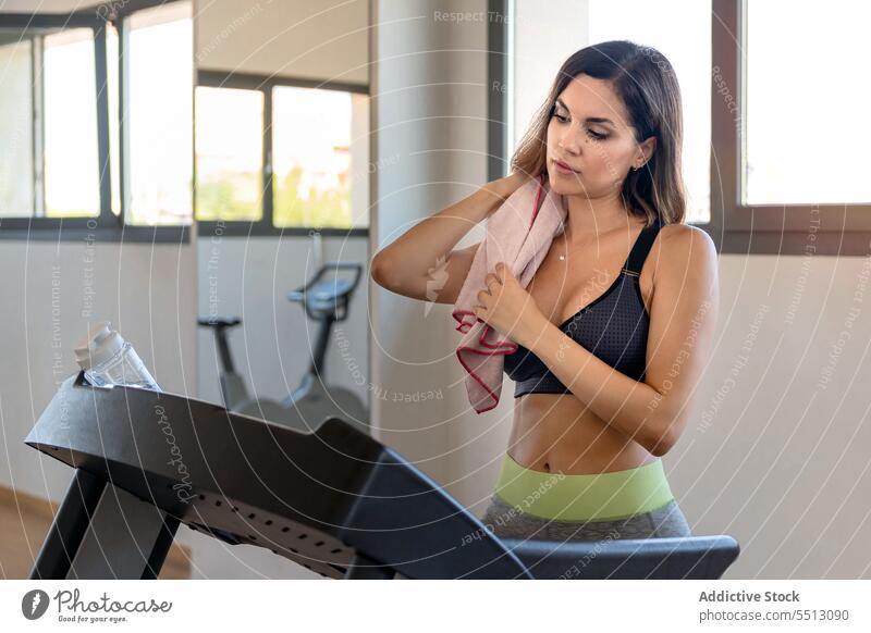 Junge Frau steht auf einem Laufband mit einem Handtuch um die Schulter müde Training Übung Schweiß Wischen passen Fitnessstudio jung Sportbekleidung Pause