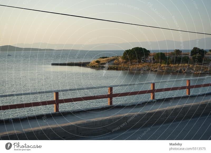 Blick von einer Brücke mit Geländer auf das Meer im Licht der Abendsonne mit Küstenlandschaft, Bucht und Halbinsel in Cunda bei Ayvalik am Ägäischen Meer in der Provinz Balikesir in der Türkei