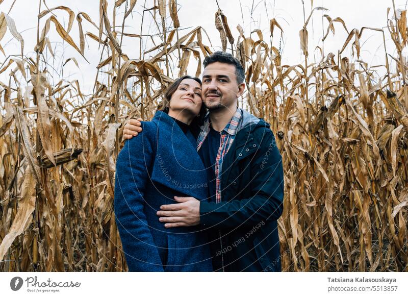 Ein junger Mann umarmt eine Frau vor der Kulisse eines herbstlichen Kornfelds Junger Mann Liebkosen Stehen Hintergrund Herbst Paar Umarmen Liebe Zuneigung