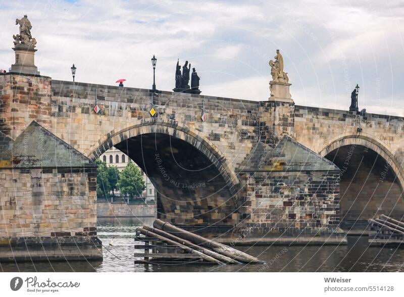 Über die berühmte alte Brücke in Prag spaziert jemand mit einem roten Regenschirm Karlsbrücke Moldau Wetter wolkig bewölkt romantisch melancholisch historisch