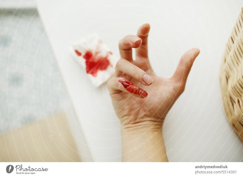 Weibliche Hand und Serviette mit rotem Blut. Frau hat sich zu Hause mit einem Messer oder einem anderen scharfen Gegenstand am kleinen Finger verletzt. Häuslicher Unfall. Blutende Wunde und Körperverletzung sind die Folge.