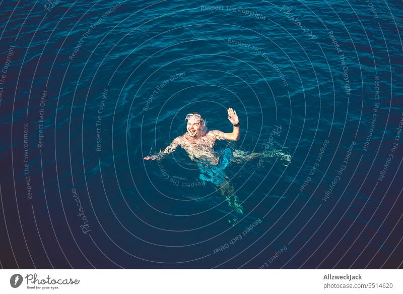 Mann mittleren Alters mit Taucherbrille auf dem Kopf winkt aus dem blauen Meer in die Kamera Meere Wasser Ozean Schwimmen & Baden baden H2O maritim heiß