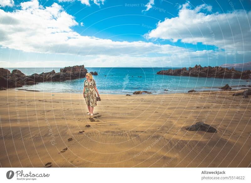 Portrait einer Frau mittleren Alters mit Sonnenbrille und Kleid an einem steinigen Strand von Lanzarote Porträt Kurzarm kurzärmelig Urlaub Urlaubsstimmung