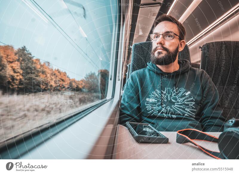 Mann reist allein mit dem Zug und schaut aus dem Fenster männlich Vollbart bärtig Brille Fotokamera Mobile Funktelefon reisen Reisender aus dem Fenster schauen