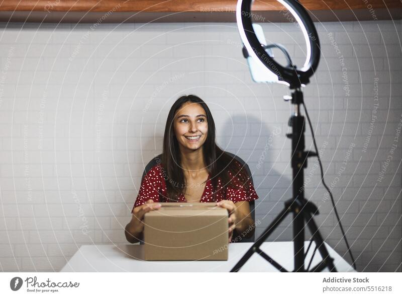 Lächelnder Vlogger beim Auspacken der neuen Lieferbox Frau Kasten vlog Blogger schießen benutzend Stativ Apparatur Video Influencer Ringlampe heiter