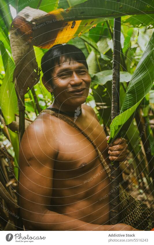 Fröhlicher ethnischer Mann mit Stock im tropischen Wald Dschungel positiv Natur kleben nackt exotisch heiter männlich Lächeln Sommer Baum Laubwerk Freude Glück