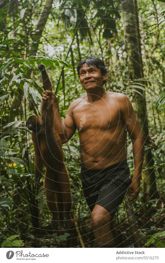 Glücklicher ethnischer Mann mit Affe im Dschungel tropisch heiter Natur Pflanze exotisch ohne Hemd männlich grün Lächeln Wald Regenwald Freude Sommer Baum