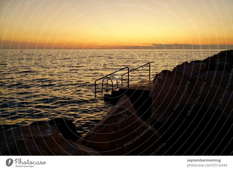 Meer in Abendstimmung Treppe führt ins Wasser Steine im Vordergrund Gelbtöne und schwarz Außenaufnahme Natur Sonnenuntergang Menschenleer