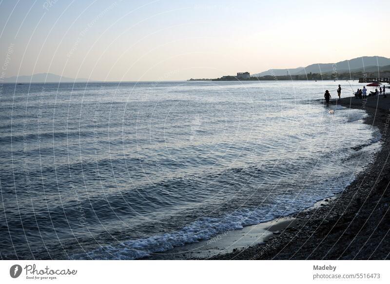 Blick vom Strand in Altinoluk mit Angler im romantischen Licht der untergehenden Sonne auf den Golf von Edremit am Ägäischen Meer in der Provinz Balikesir in der Türkei