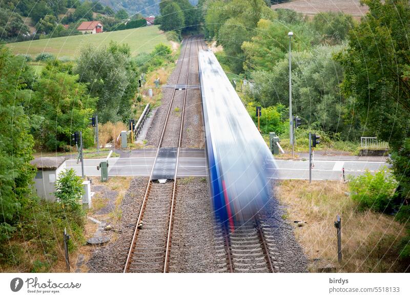 fahrender Zug kreuzt eine Straße am Bahnübergang. Bewegungsunschärfe Personenzug Gleise Schienenverkehr Öffentlicher Personennahverkehr Eisenbahn Schienennetz