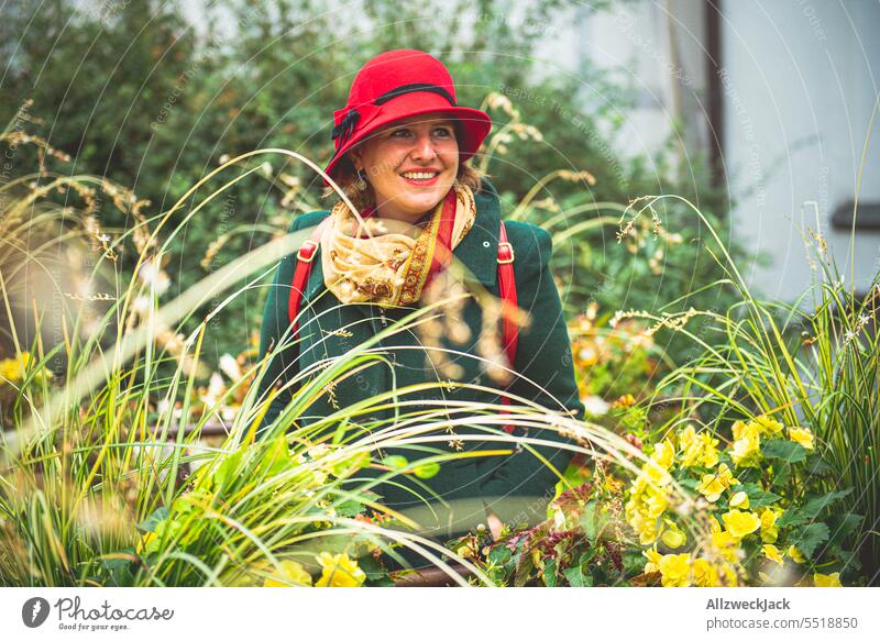 junge Frau mit grünem Mantel und rotem Hut zwischen Gräsern und Grünpflanzen Herbst herbstlich deutschlandreise sympathisch adrett modisch Außenaufnahme Porträt