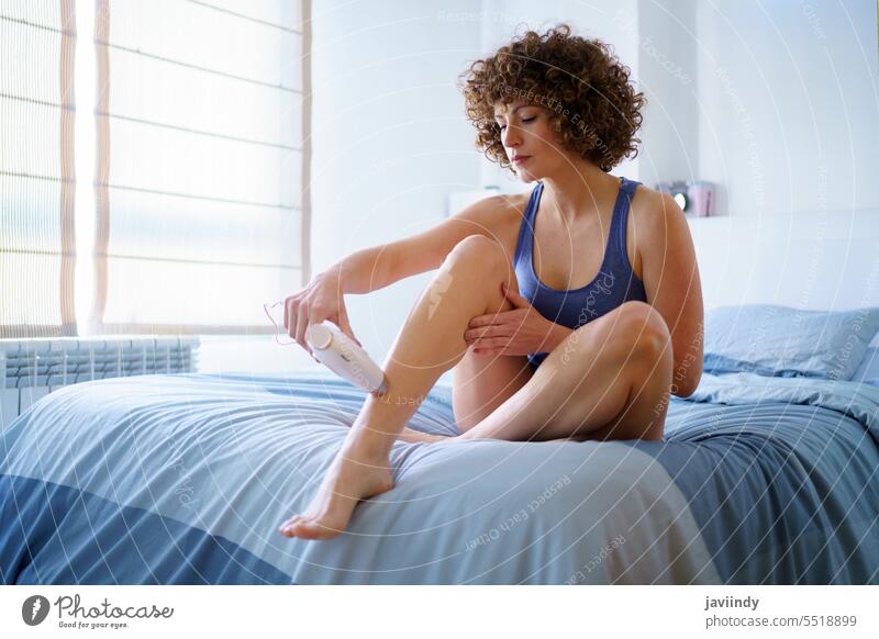 Erwachsene Frau bei der Laser-Haarentfernung am Bein auf dem Bett ipl Laser mit gepulstem Licht entfernen Behaarung Schlafzimmer Nachtwäsche benutzend