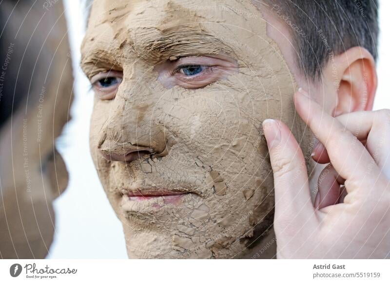 Eine Frau berührt liebevoll das Gesicht eines Mannes mit Schönheitsmaske berühren Maske Heilerde anfassen Finger Liebe zusammen Paar Gesundheit Berührung braun