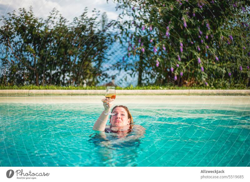 junge Frau im Pool hält ein Glas Weißwein in die Höhe während ihr das Wasser bis zum Hals steht Junge Frau hübsch sympathisch schön Erfrischung