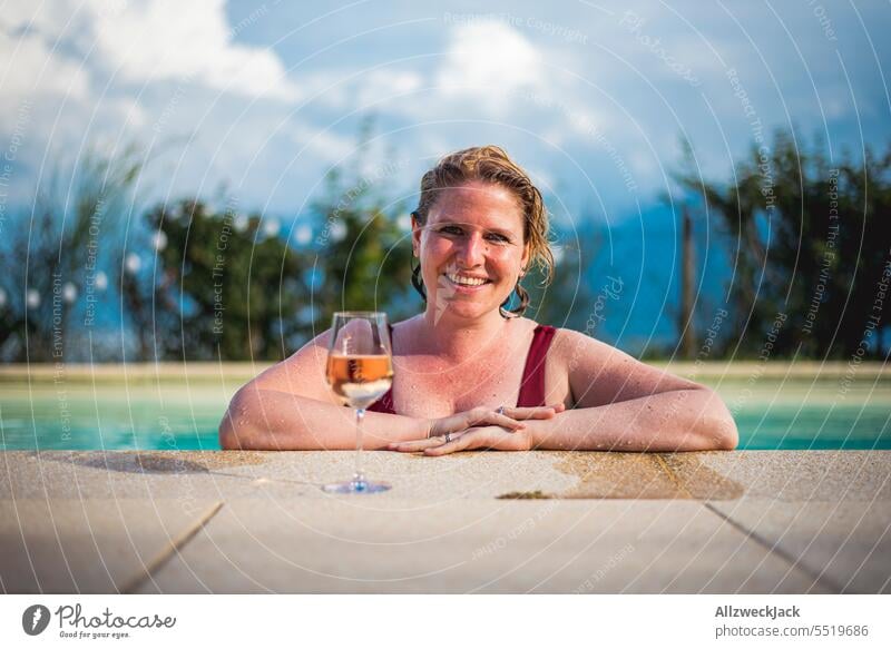 junge lächelnde Frau mit nassen Haaren lehnt am Poolrand mit einem Glas Weißwein Junge Frau hübsch sympathisch schön Erfrischung Erfrischungsgetränk Wein