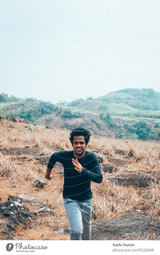 ein junger Mann rennt einen Hügel hinauf in einem schwarzen Shirt. Natur grün Himmel Wiese blau Landschaft Gras Außenaufnahme Umwelt Feld Schönes Wetter Gebirge