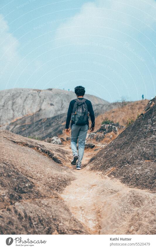 ein junger Mann mit einem Rucksack auf dem Rücken wandert in den Bergen mit felsigen, grossen Steinen wandern laufen Backpacker Berge u. Gebirge Tourismus