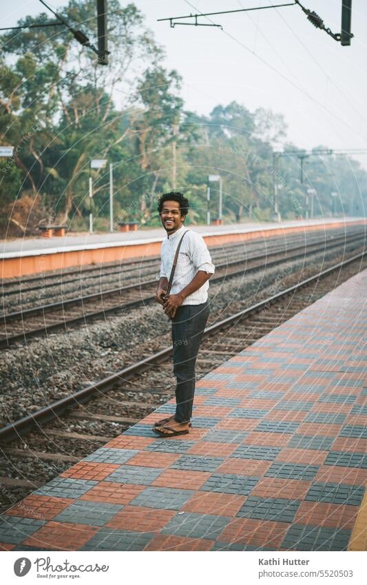 ein junger Mann steht am Bahngleis und wartet auf den Zug. Ein lachen ist auf seinem Gesicht Bahnhof Bahnsteig warten Verkehr Eisenbahn Ferien & Urlaub & Reisen