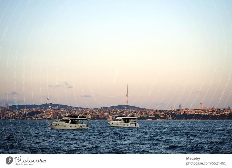 Motorboote und Yachten vor der Anlegestelle der Fähre über den Bosporus in Karaköy in Licht der untergehenden Sonne mit Blick auf den Fernsehturm Küçük Çamlıcaim in Istanbul in der Türkei