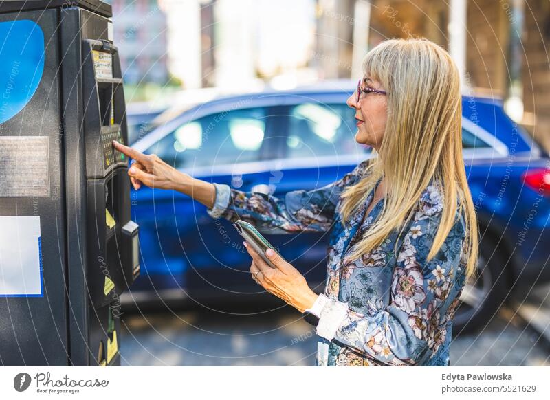 Ältere Frau benutzt ein Mobiltelefon, um für einen Parkplatz in der Stadt zu bezahlen natürlich genießen zufrieden heiter selbstbewusst Freude Rentnerin