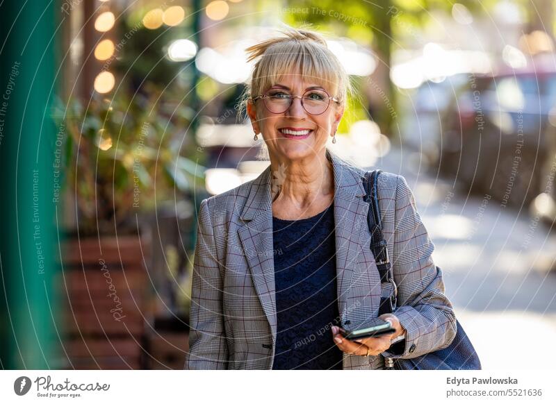 Porträt einer lächelnden älteren Frau mit Mobiltelefon auf der Straße natürlich genießen zufrieden heiter selbstbewusst Freude Rentnerin im Freien außerhalb