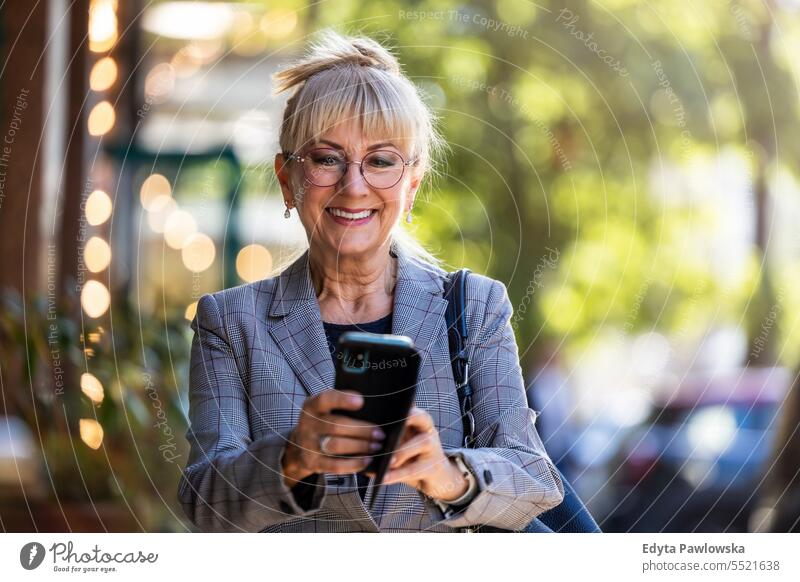 Porträt einer lächelnden älteren Frau mit Mobiltelefon auf der Straße natürlich genießen zufrieden heiter selbstbewusst Freude Rentnerin im Freien außerhalb