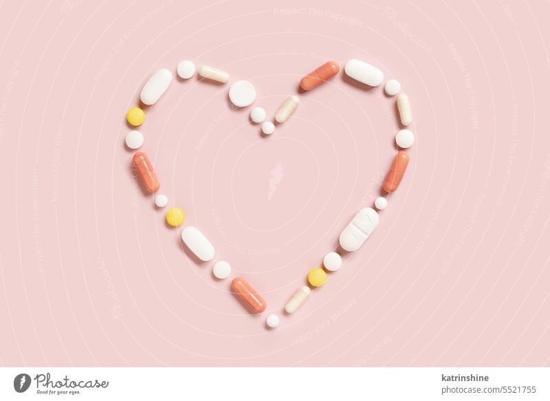 Herzform aus bunten Medikamentenpillen und Kapseln auf hellrosa, Ansicht von oben Form Linie Pillen Draufsicht Pharma Kardiologie Behandlung Krankheiten Medizin