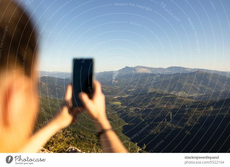 Eine glückliche junge Frau fotografiert die Landschaft mit ihrem Smartphone vom Gipfel eines Berges aus. Natur reisen Himmel Ansicht im Freien Schönheit Wald