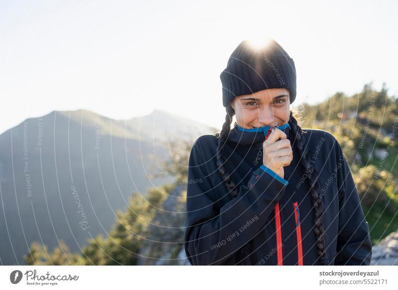 Eine junge Frau, Bergsteigerin, geschützt vor der Kälte auf dem Gipfel eines Berges, lächelt und genießt die Landschaft und den Moment in der Natur Person