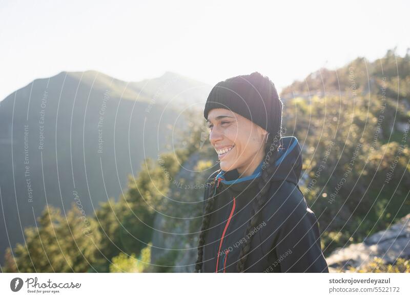 Eine junge Frau, Bergsteigerin, geschützt vor der Kälte auf dem Gipfel eines Berges, lächelt und genießt die Landschaft und den Moment in der Natur Lifestyle