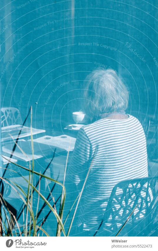 Jemand sitzt in einem Straßencafé in der Sonne und trinkt Kaffee beim Lesen Durchblick Café Frau ältere Dame grauhaarig gestreift Streifen blau türkis