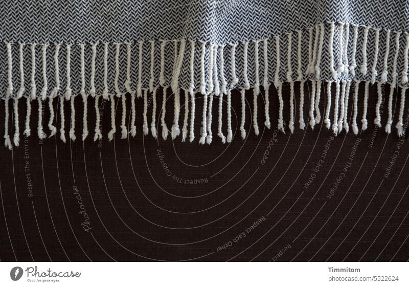 Decke mit Anhang auf einem Sofa Muster Textil Gewebe Stoff Design grau braun Textfreiraum unten Menschenleer Farbfoto Falten