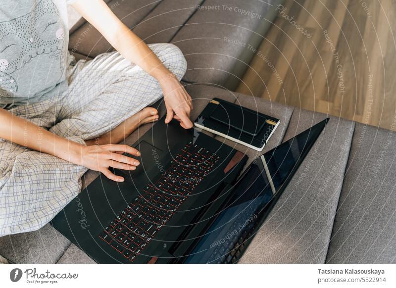 Eine junge Frau im Pyjama sitzt auf der Couch und benutzt einen Laptop Technik & Technologie Lebensstile Fernarbeit Notizbuch Telefon WiFi Computer Menschen