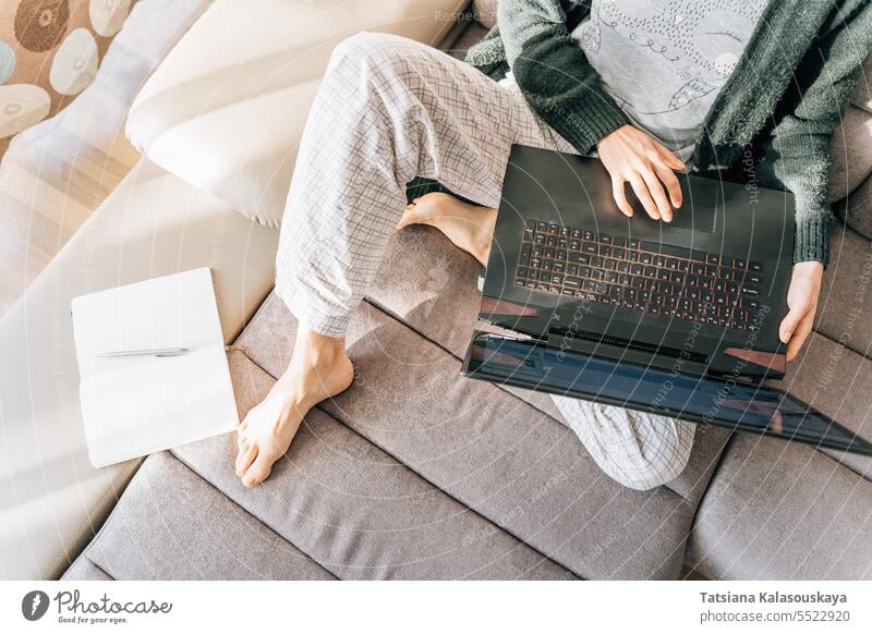 Eine Frau in Hauskleidung mit einem Laptop, daneben liegen ein Notizbuch und ein Stift online Internet Lebensstile Fernarbeit WiFi Computer