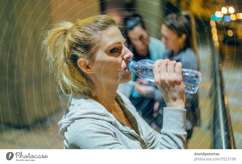 Porträt einer müden Läuferin, die nach einem nächtlichen Training mit ihren Freunden in der Stadt Wasser trinkt. Frau trinken durstig Übung rennen liquide