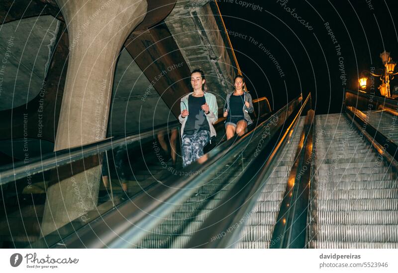 Frauen Freunde Ausbildung laufen unten Rolltreppe in der Stadt in der Nacht rennen Training Läufer Mechaniker Treppe Treppenhaus Schritt nach unten Großstadt