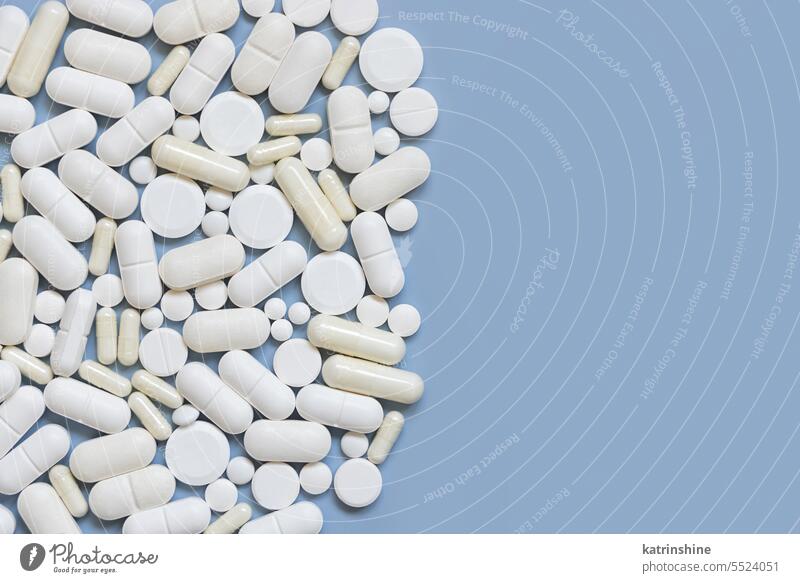 Mischung aus weißen medizinischen Kapseln und Pillen auf hellblauer Draufsicht, Kopierraum. Medizinische Behandlung mischen Pharma Textfreiraum Borte Sortiment