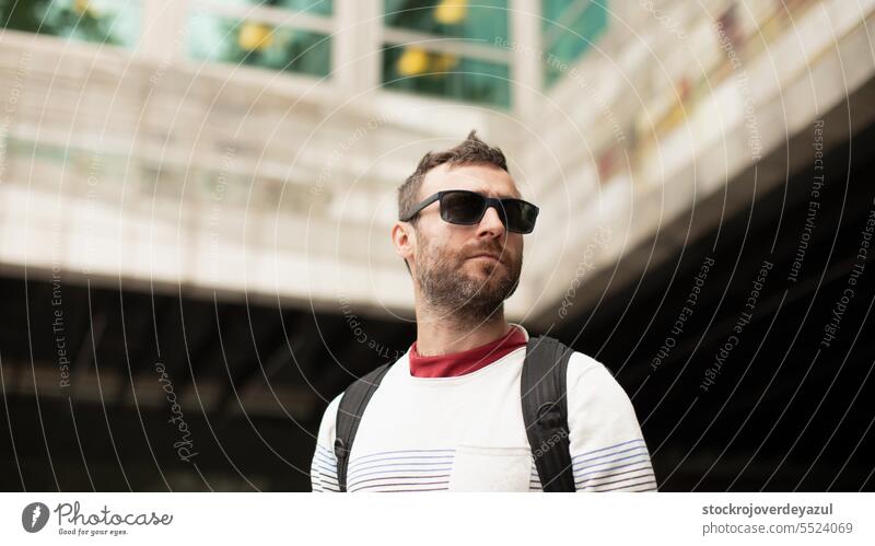 Ein junger, reisender Mann mit Sonnenbrille beobachtet die Stadt und die Bürogebäude während eines Spaziergangs in Spanien. Person Männer männlich Erwachsener