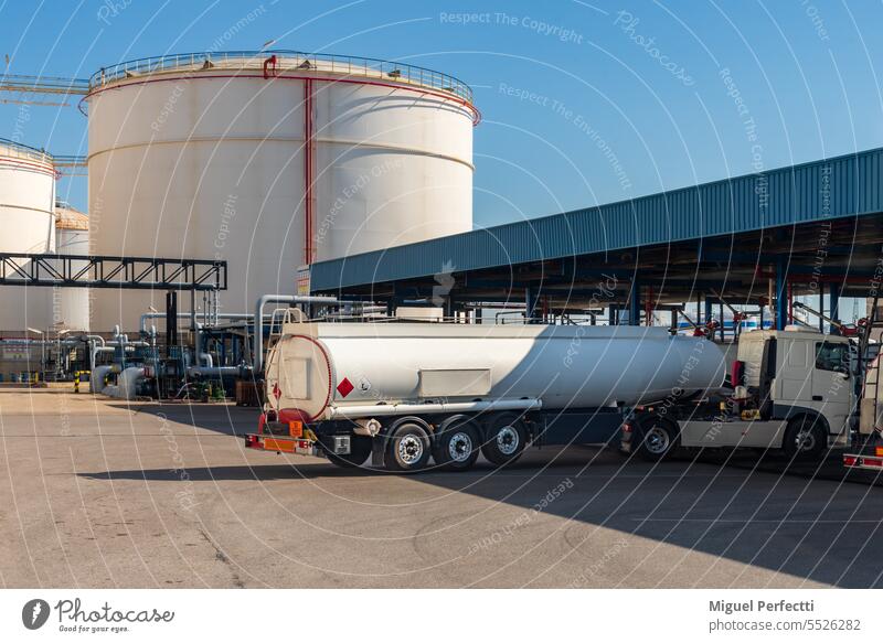 Ein Tankwagen fährt zum Beladen an einer Laderampe ein, mit den großen Lagertanks im Hintergrund. Lastwagen Brennstoff Verkehr brennbar Terminal Beladung Fabrik
