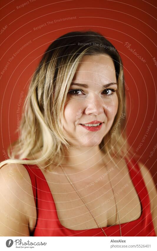 Portrait einer blonden, schönen, lächelnden Frau in einem roten Kleid vor einer roten Wand langhaarig lange Haare Gesicht natürlich authentisch attraktiv