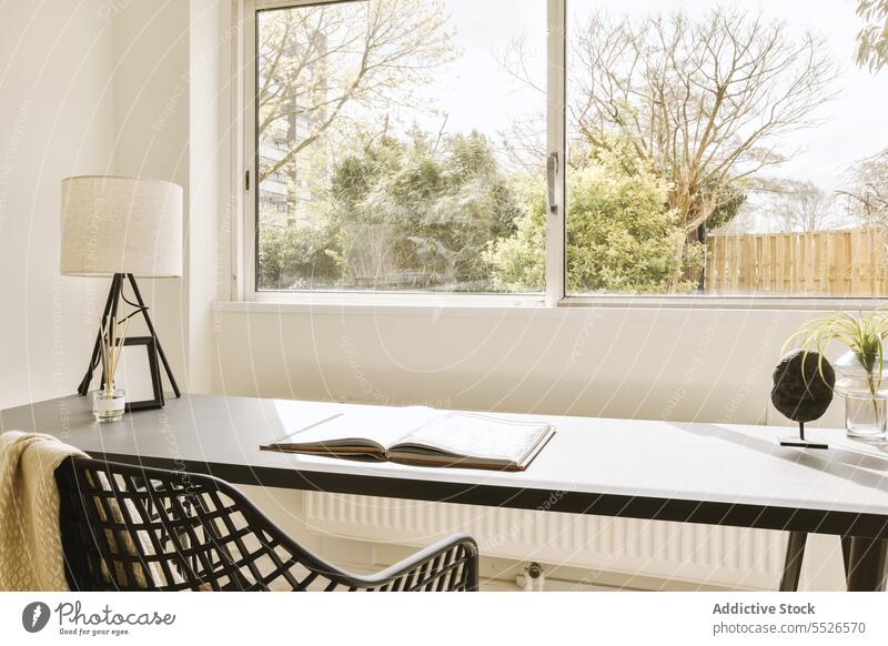 Heimbüro mit Buch und Lampe auf dem Schreibtisch vor dem Fenster klein Pflanze Stuhl Glas groß hell Licht Sonnenlicht Bildung weiß Wand Textfreiraum Büro Haus