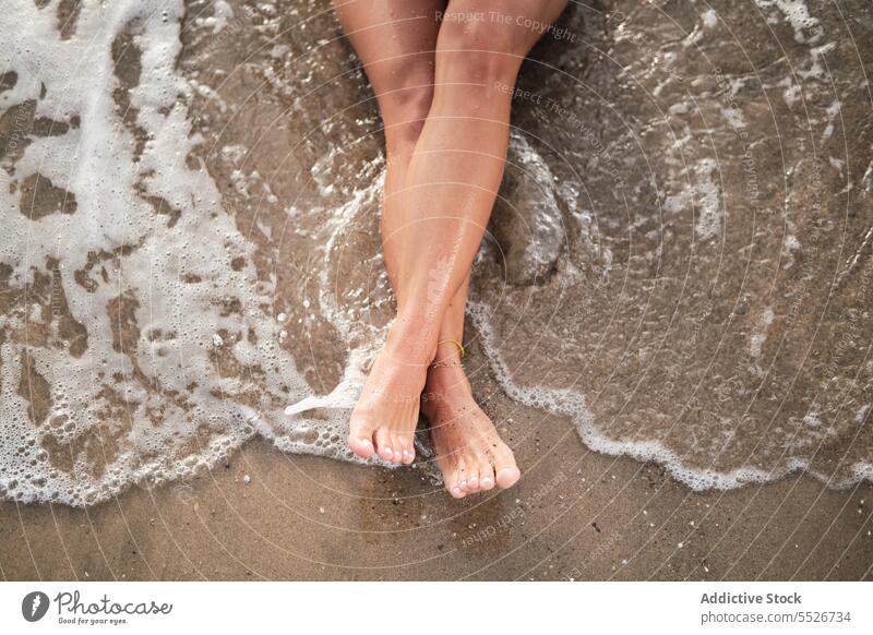 Crop Beine der Frau entspannen auf nassen Sandstrand Barfuß Strand Urlaub Sommer schäumen Wasser MEER ruhen sich[Akk] entspannen Küste Ufer Erholung Meeresufer